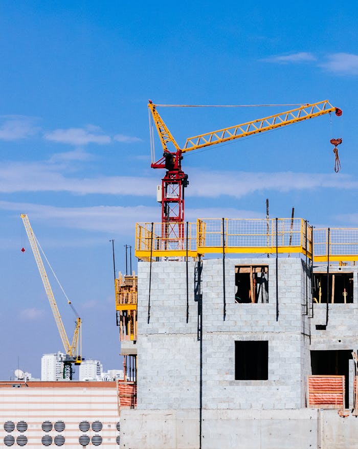 Mastering the First Impression: Your intriguing post title goes here Tower cranes at a construction site working on a high-rise building under a clear blue sky.
